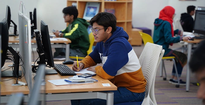 a cs student writing on a pad while looking at the screen 