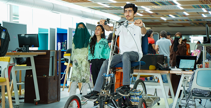 Student tests robotic vehicle prototype while Robotics Engineer observes in a university makerspace.